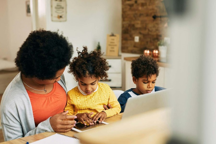 A parent working through paperwork at the kitchen bench with two children