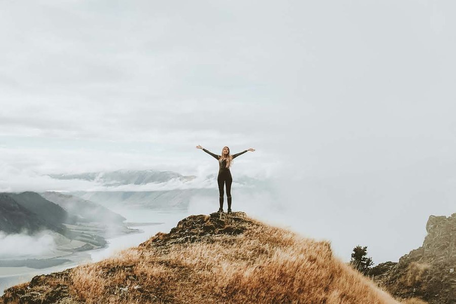 A person standing on a hilltop with arms outstretched, looking out over the horizon