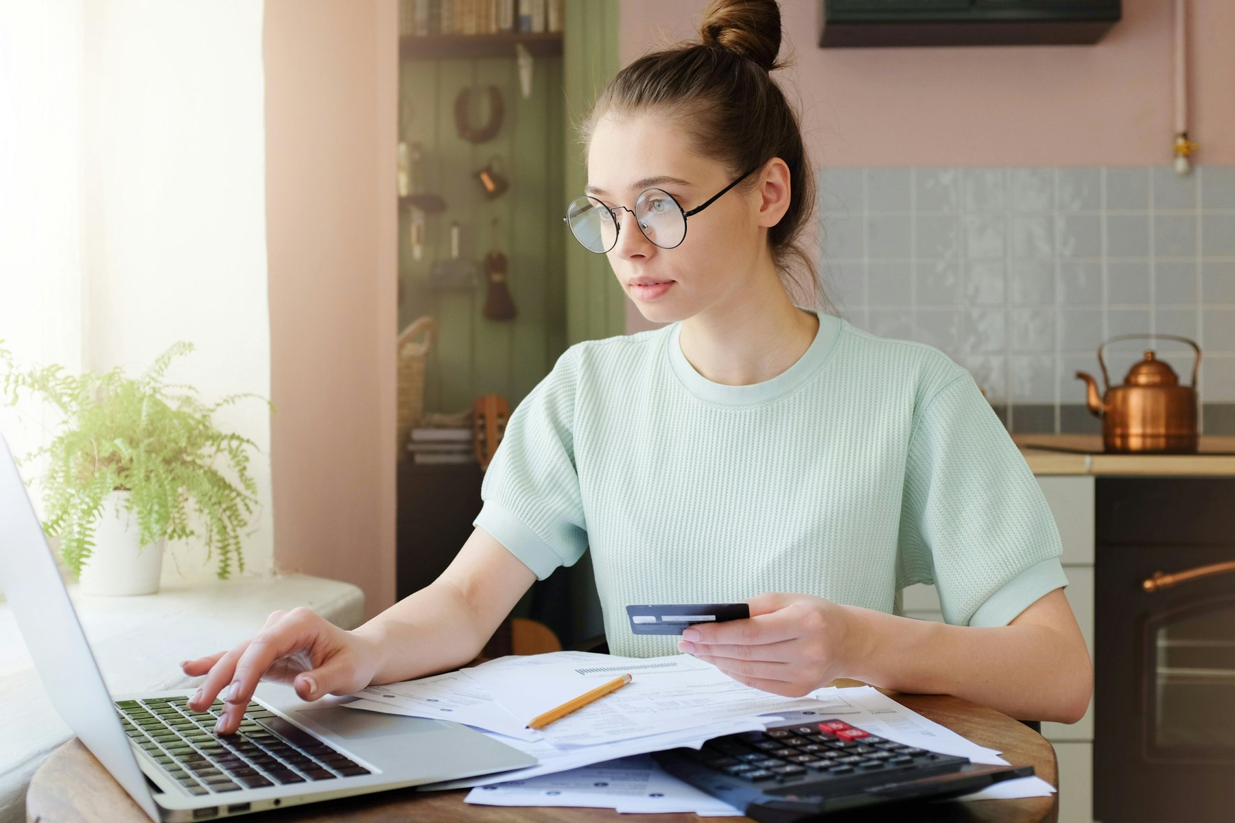 A person working through their household finances at a laptop with paperwork and a calculator