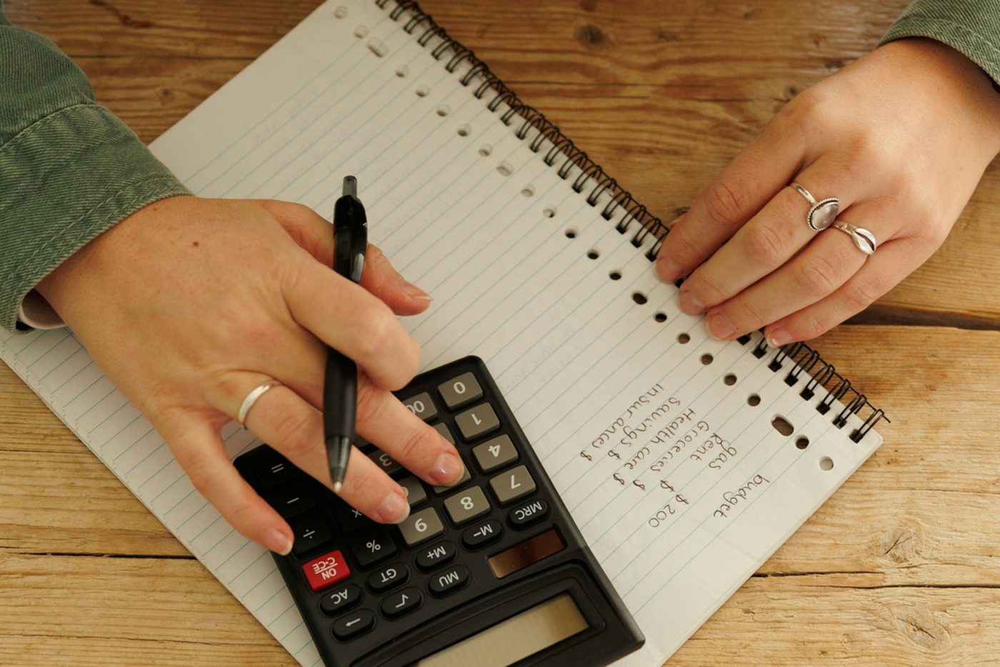 Hands using a calculator beside a ruled notebook on a wooden table