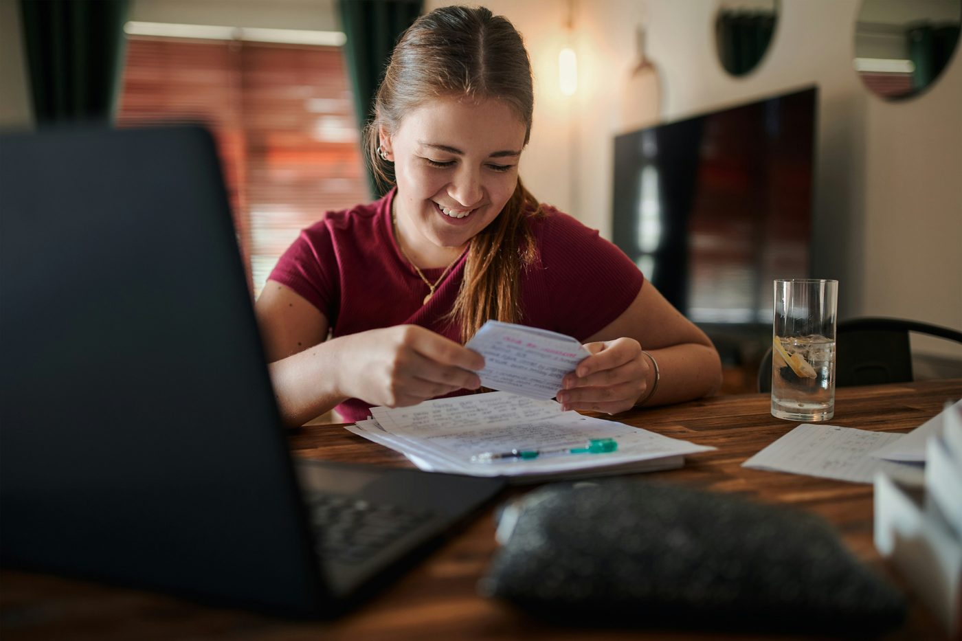 A young woman smiling as she reads a statement beside her laptop