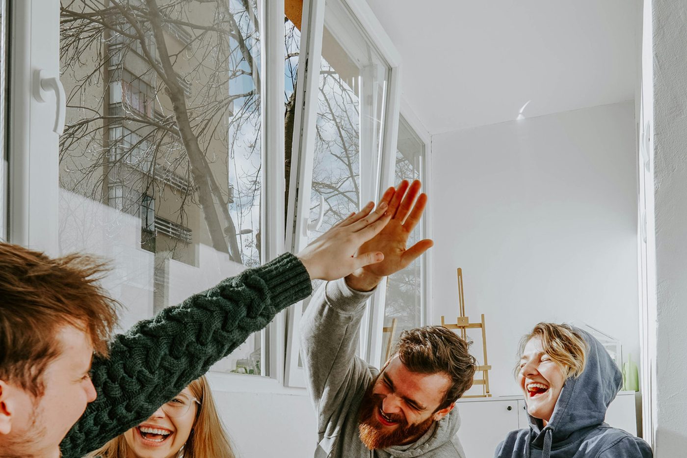 Three friends laughing and high-fiving by a window