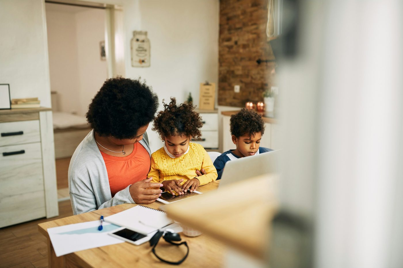 A parent and two children working through paperwork at a kitchen bench
