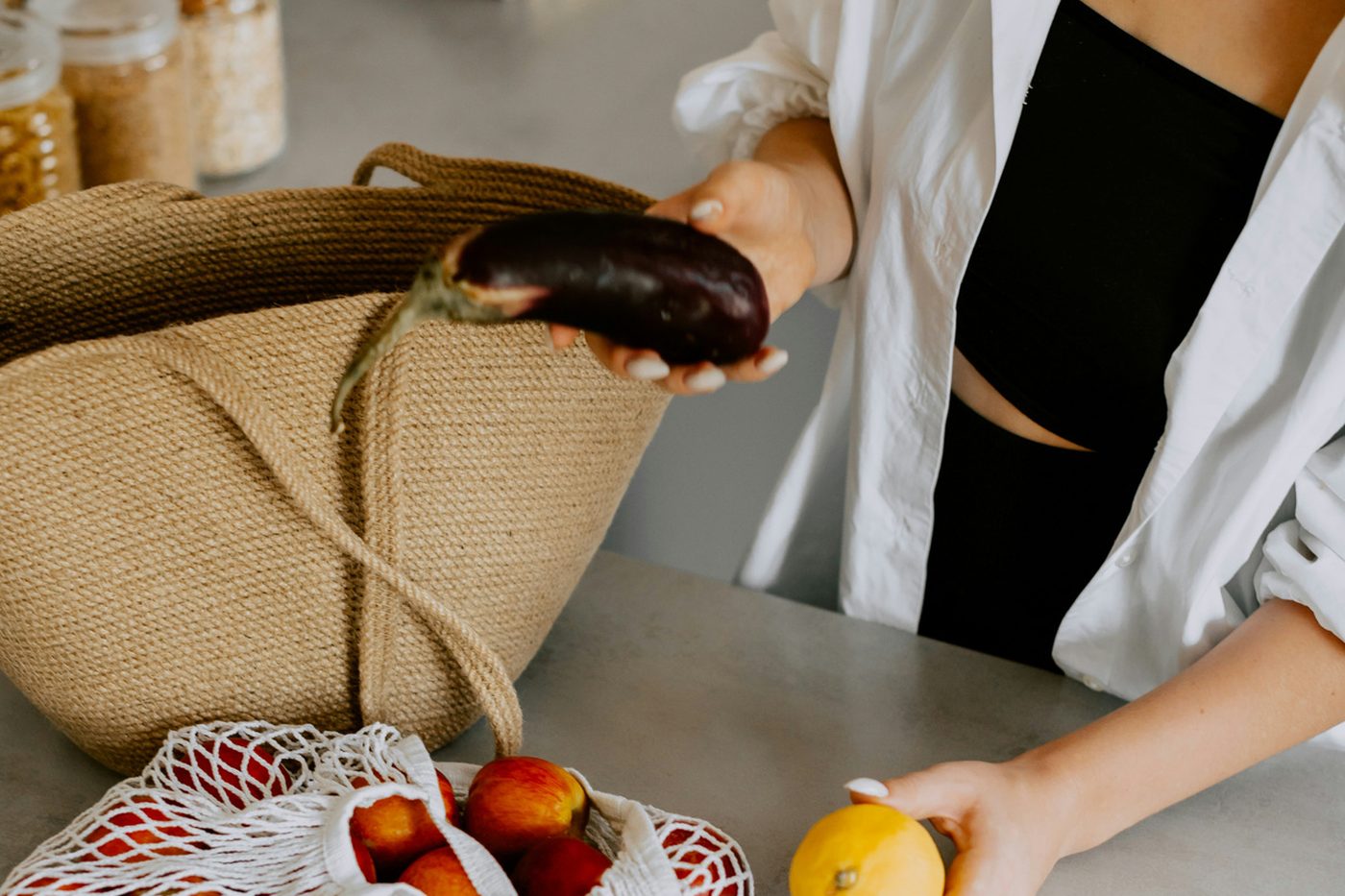 A shopper unpacking fruit and vegetables from a mesh bag onto a bench