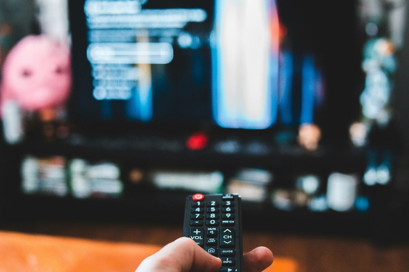 A hand holding a remote in front of a television showing a streaming menu