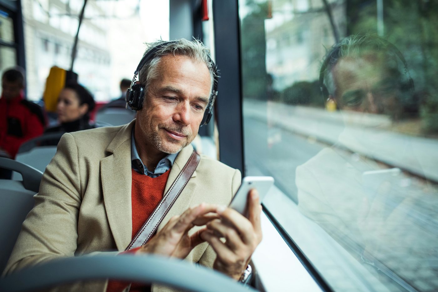 A commuter with headphones looking at his phone on a bus